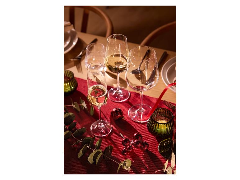 Table de fête avec verres à vin, décorations rouges et verdure sur une nappe rouge.