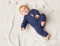 Un bébé allongé sur une couverture blanche, portant une combinaison bleue avec un lapin dessus.