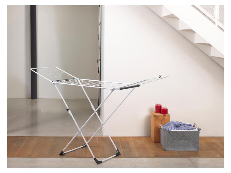 Séchoir à linge blanc avec panier à linge gris et bougies rouges.