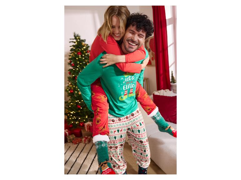 Couple joyeux en pyjamas de Noël, l'homme porte la femme sur son dos près d'un sapin de Noël.