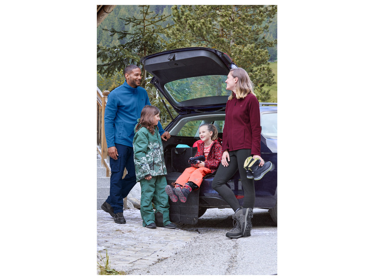 Une famille avec des vestes en polaire et des chaussures de randonnée près d'une voiture.