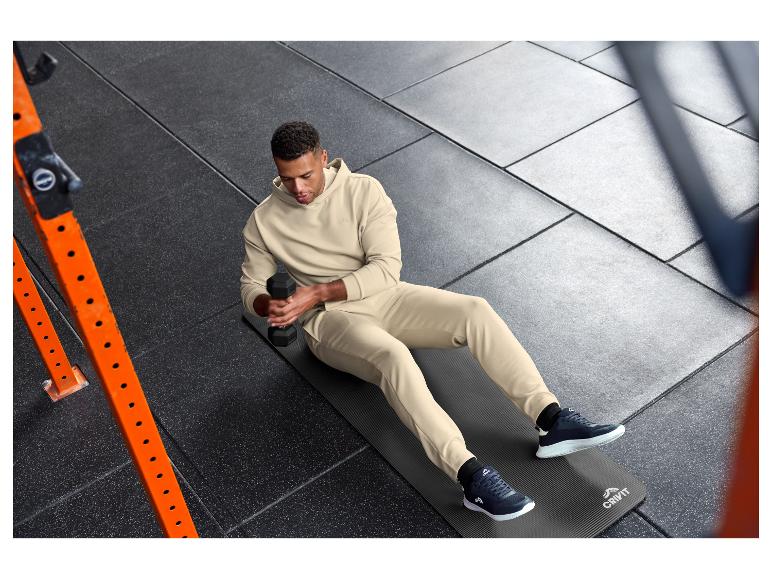 Homme en survêtement beige s'exerçant avec un haltère sur un tapis CRIVIT.