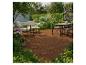 Terrasse en bois avec mobilier de jardin, comprenant un ensemble repas et des fauteuils, entourée de verdure.