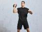 Un homme en t-shirt et short noirs fait un exercice avec un kettlebell.