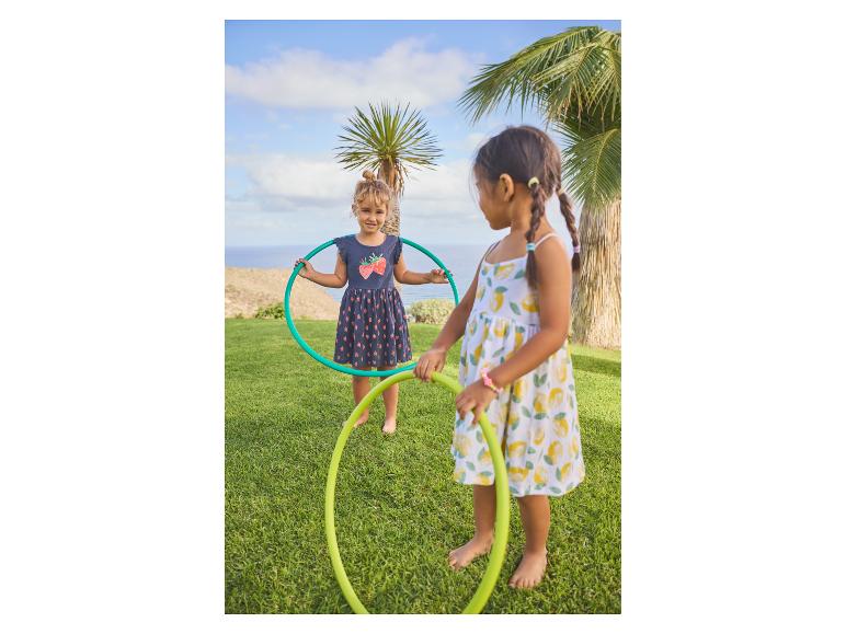 Deux petites filles jouent avec des cerceaux sur l'herbe, avec des palmiers et la mer en arrière-plan.
