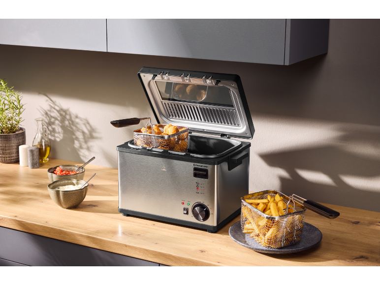 Friteuse en acier inoxydable avec nuggets de poulet et frites dans une cuisine.