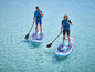 Deux personnes pagayent sur des planches de paddle gonflables bleues Red Paddle Co. dans une eau turquoise.