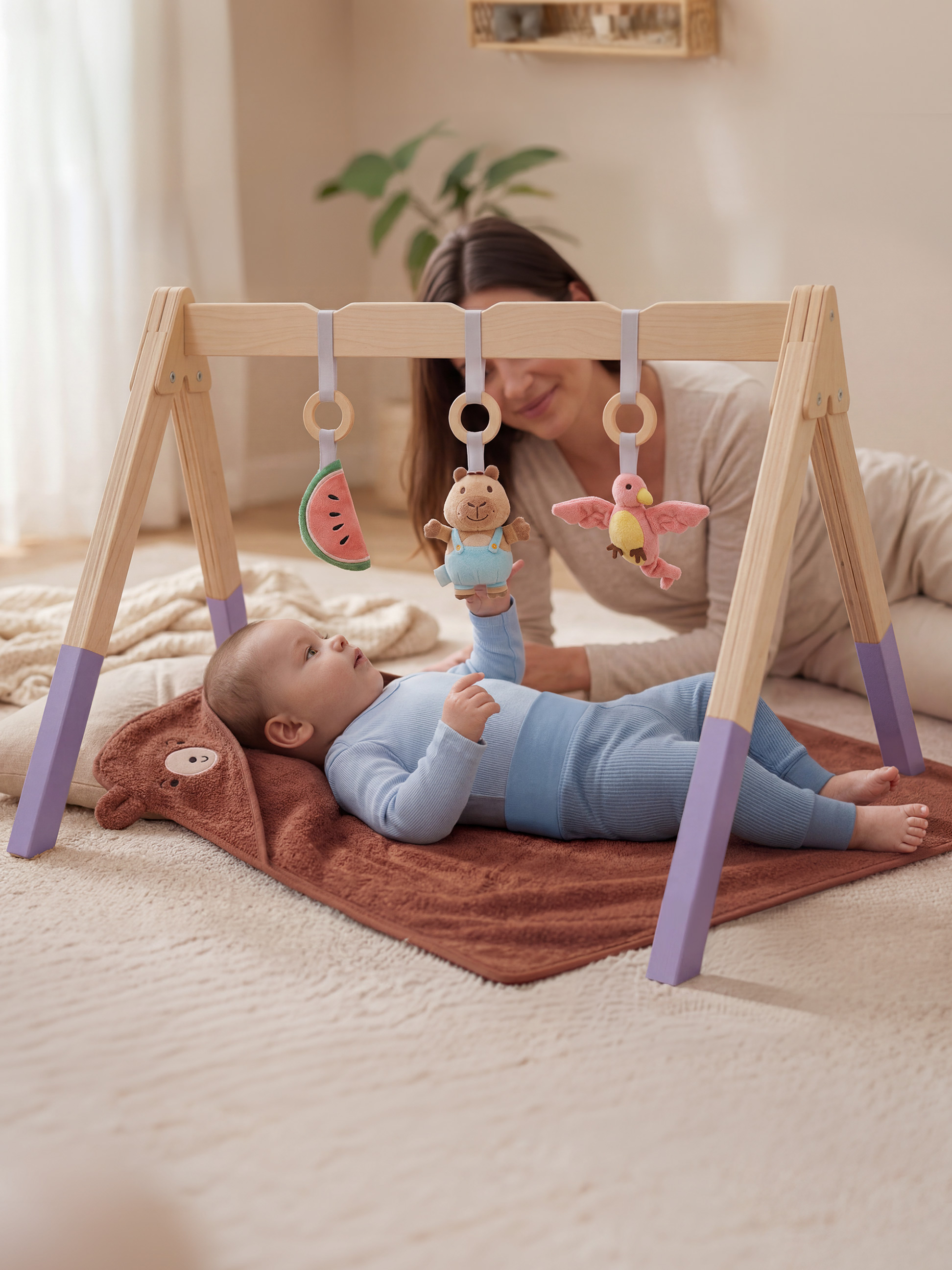 Bébé jouant avec un portique d'éveil en bois avec des jouets suspendus, maman en arrière-plan.