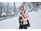 Femme avec des jumelles et une veste rose dans un paysage hivernal enneigé.