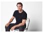 Un homme en t-shirt et pantalon noirs est assis sur une chaise transparente.