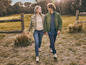 Une femme et un homme marchent main dans la main sur un champ d'herbe, ils portent tous les deux des manteaux d'hiver.