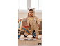Bébé souriant en barboteuse et cardigan avec lapin, à côté d'un vélo en bois.