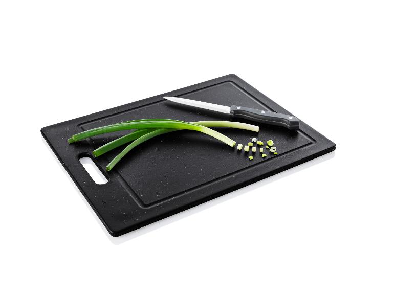 Une planche à découper noire avec des oignons verts, un couteau et des oignons coupés.