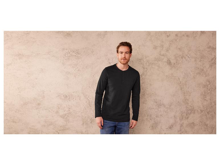 Un homme porte un t-shirt noir à manches longues et un jean bleu.