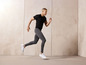 Homme en t-shirt noir et pantalon de survêtement gris courant en baskets blanches.