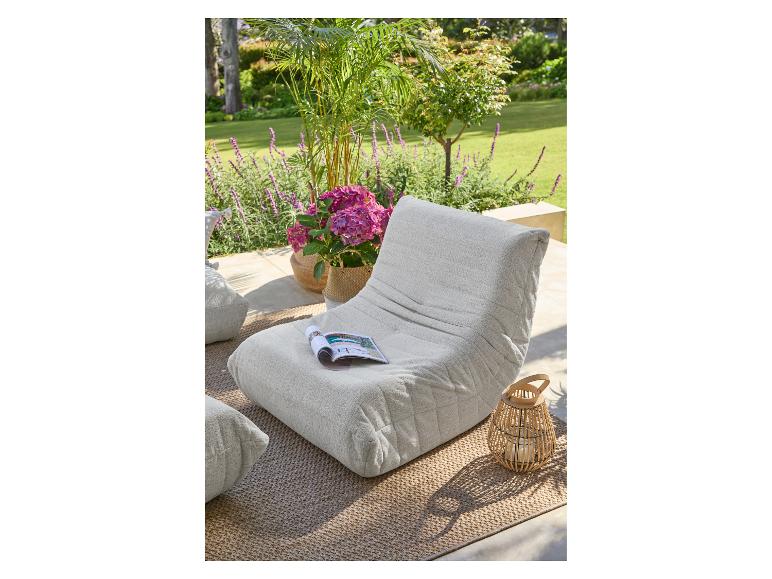 Pouf d'extérieur beige avec magazine, plantes et lanterne sur un tapis.