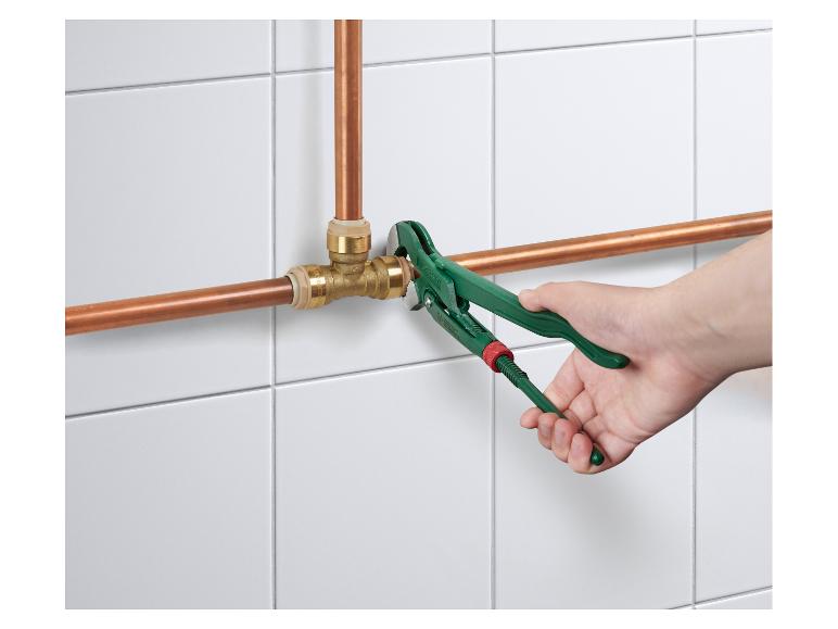 Une main utilise une clé à molette verte pour serrer un raccord sur des tuyaux en cuivre.