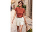 Une femme en t-shirt orange et short blanc marche dans la rue.