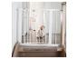 Bébé assis derrière une barrière de sécurité blanche en haut d'un escalier en bois.