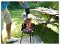 Homme versant des charbons ardents dans un barbecue au charbon de bois dans le jardin, table de pique-nique en arrière-plan.