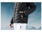 Une veste en duvet noire et un pantalon de ski blanc sur fond de montagnes.