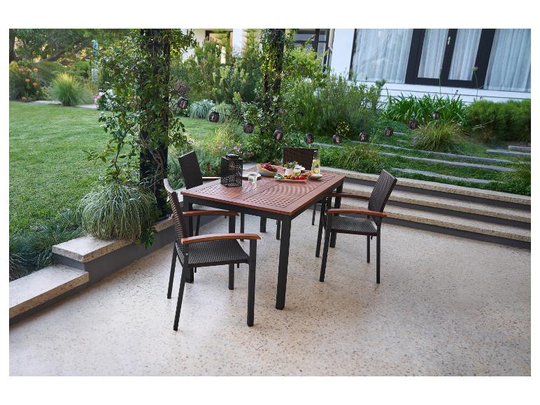 Ensemble de salle à manger extérieur avec table en bois et chaises en osier sur une terrasse avec vue sur le jardin.