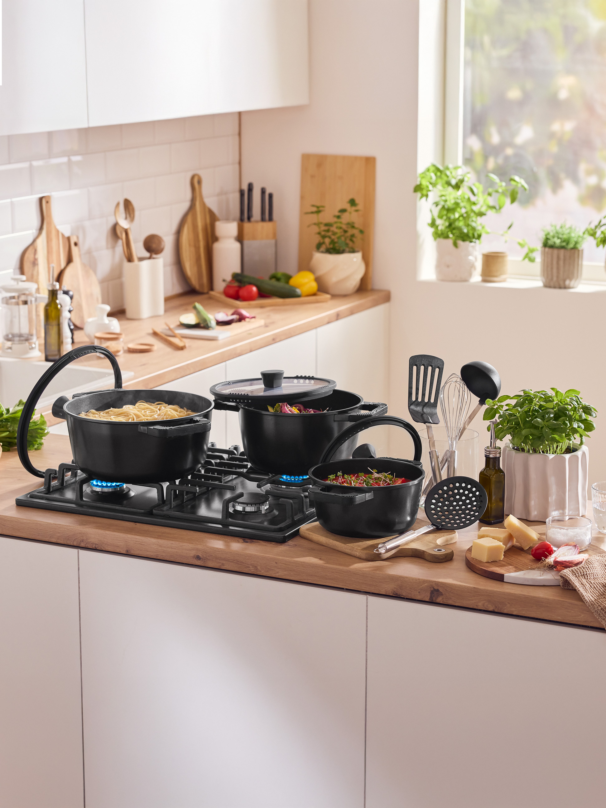 Plan de travail de cuisine avec casseroles sur la cuisinière, ustensiles et ingrédients frais.