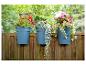 Trois jardinières bleues avec des fleurs colorées suspendues à une clôture en bois.