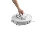 Une main retirant le bac à poussière d'un robot aspirateur blanc
