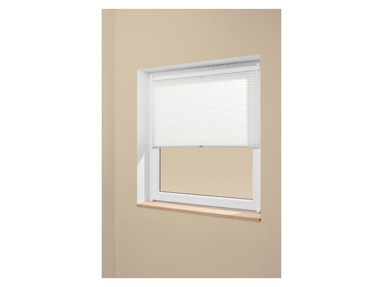 Store plissé blanc couvrant la moitié supérieure d'une fenêtre avec un rebord en bois.