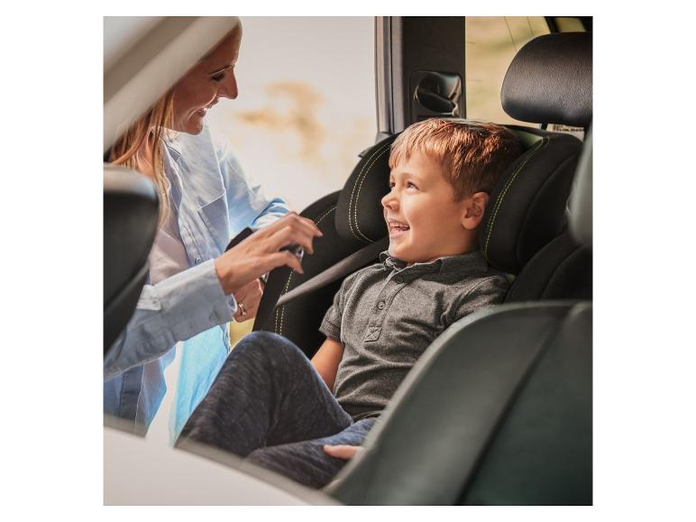 Une femme souriante attache un enfant dans un siège auto pour enfant.