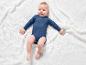 Un bébé dans un body bleu sur une couverture blanche en tricot.