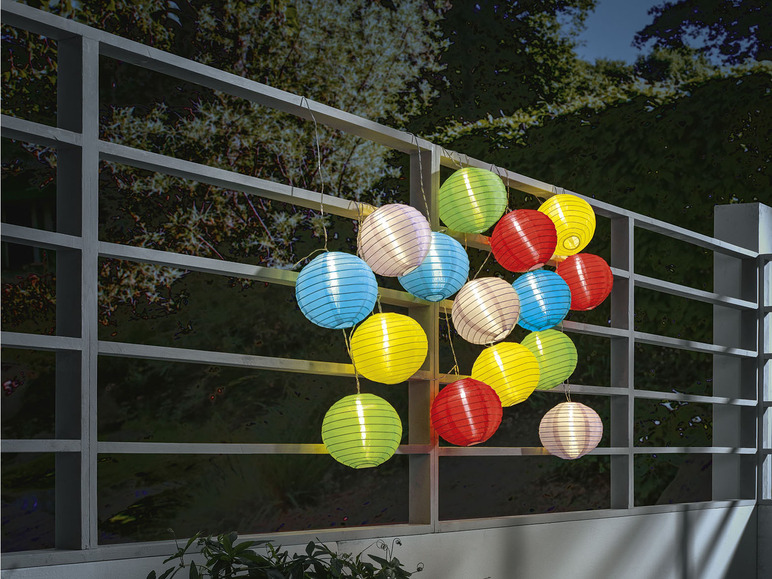 Une guirlande de lampions ronds de couleurs accrochés à une clôture.