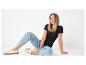 Femme en t-shirt noir et jean bleu clair, assise par terre, souriante.