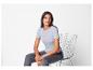 Une femme portant un t-shirt bleu clair et un pantalon gris, assise sur une chaise en métal.
