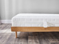 Un matelas blanc avec un cadre de lit en bois sur un plancher en bois.