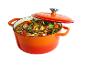 Cocotte orange remplie d'un ragoût de viande et de légumes variés, avec le couvercle partiellement posé.