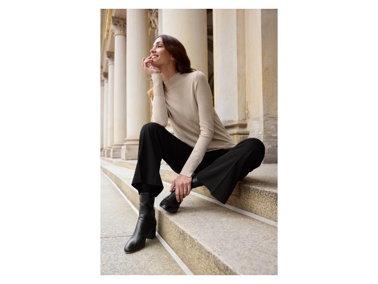 Une femme portant un pull beige, un pantalon noir et des bottes noires.