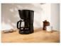 Cafetière filtre noire avec verseuse en verre, tasse et biscuits sur une table en bois.