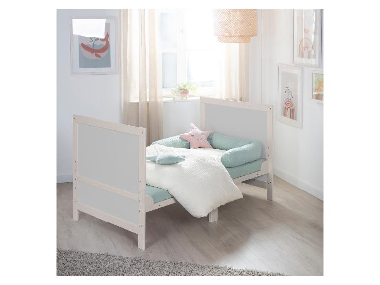 Lit bébé en bois blanc avec literie vert menthe et oreillers en forme d'étoile dans une pièce lumineuse.