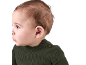 Gros plan d'un bébé en pull tricoté vert, regardant à gauche.