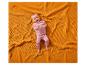 Bébé heureux en vêtements roses allongé sur une couverture gaufrée orange.