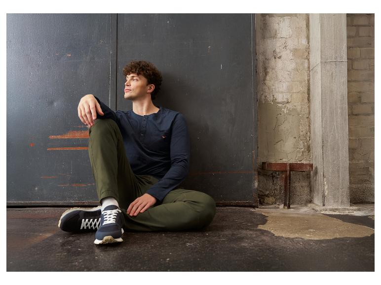 Homme en t-shirt à manches longues bleu marine et pantalon vert, assis par terre.