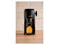 Machine à glace pilée noire avec de la glace orange dans un verre sur une table en bois.