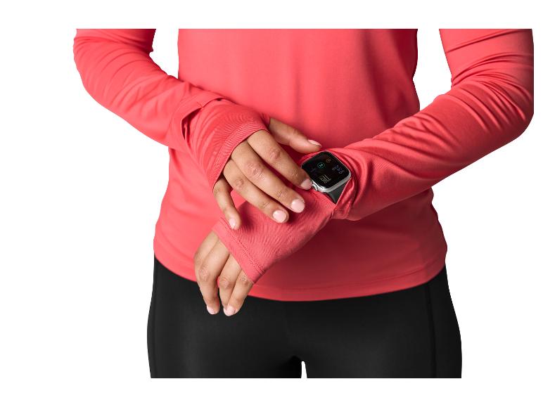 Femme en haut corail à manches longues avec passe-pouces, vérifiant une montre connectée à son poignet.