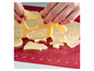 De la pâte à biscuits est découpée en différentes formes sur un tapis de cuisson rouge.