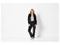 Une femme porte un pantalon de survêtement et un sweat-shirt noirs.