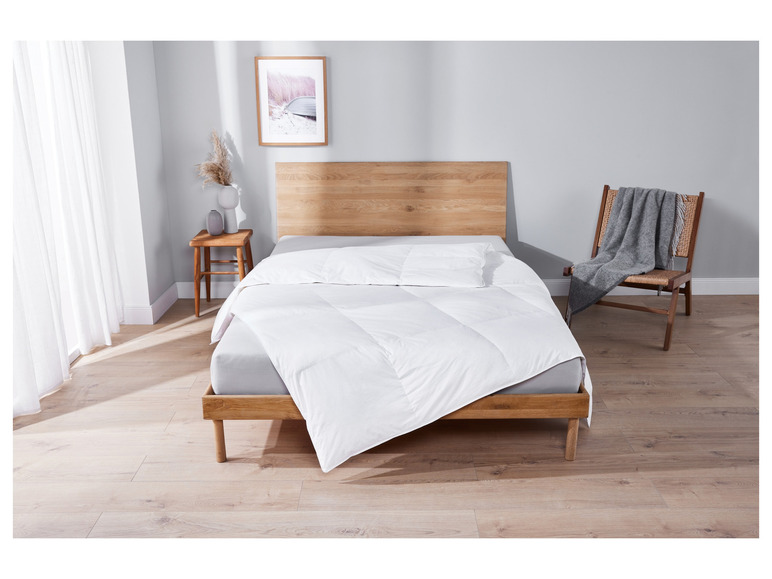 Une couette blanche sur un cadre de lit en bois dans une chambre claire.