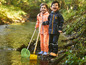 Deux enfants vêtus de vêtements de pluie jouent avec un filet et une pelle dans un ruisseau.