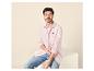 Homme en chemise rose et jean bleu assis sur un cube blanc.